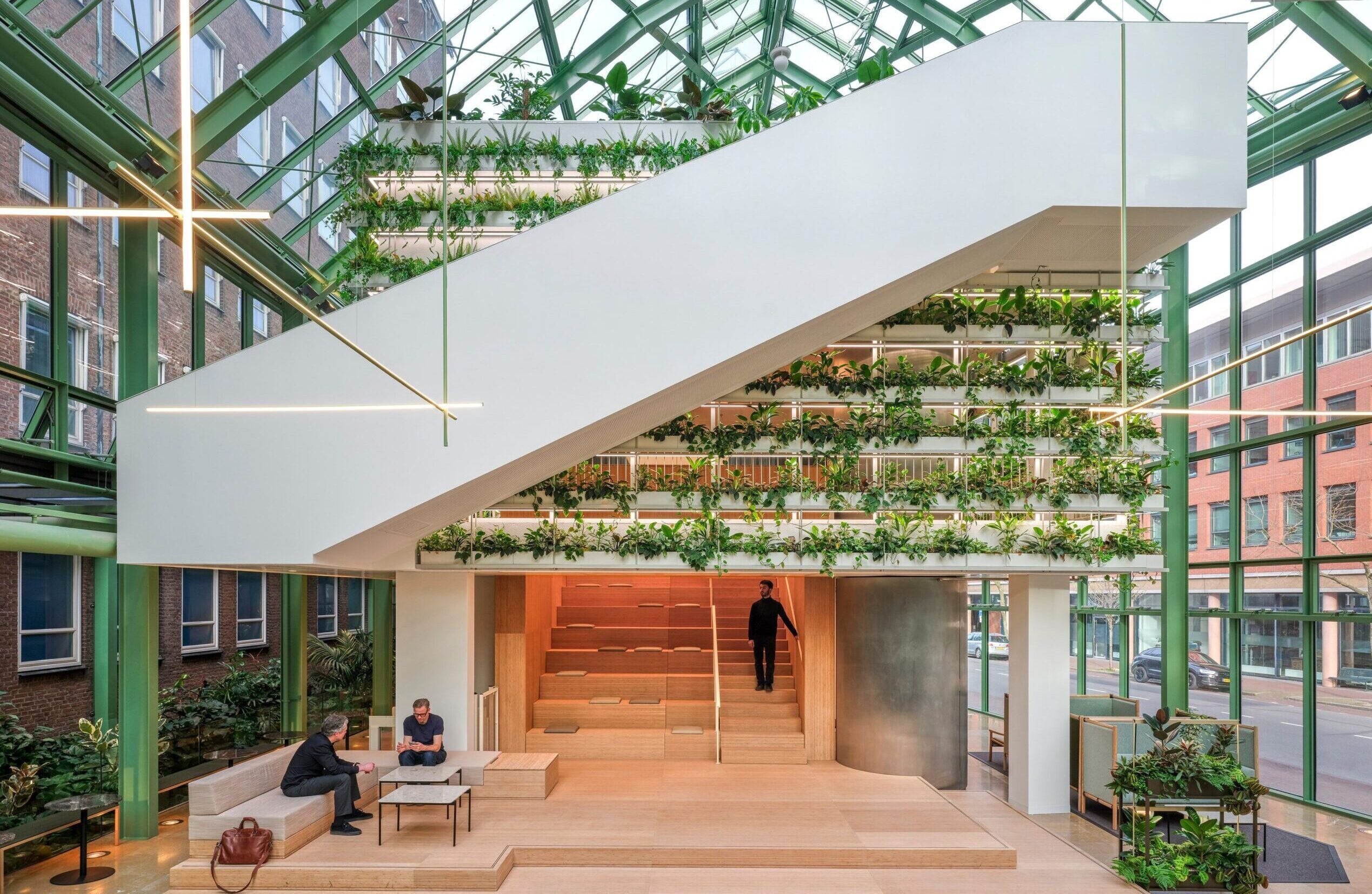 Central atrium featuring a sculptural pavilion clad in vertical timber slats beneath a green steel-framed glass roof.