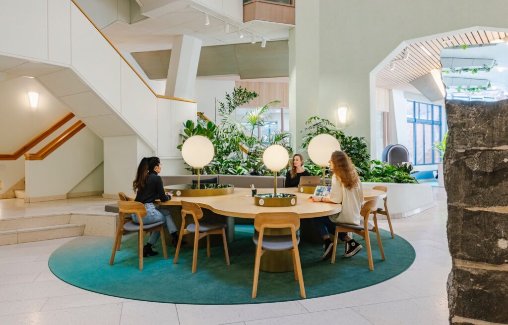 Centrale werk- en ontmoetingsplek met ronde tafel en interieurbeplanting in het Zandkasteel Amsterdam.