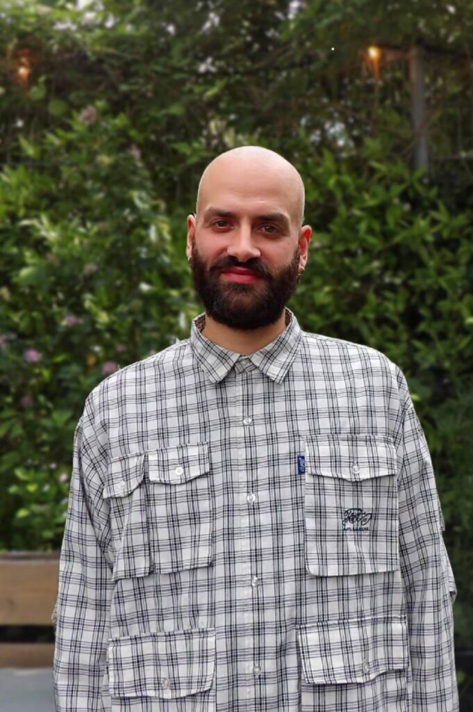 Smiling portrait of Francesco Carrasso from MOSS, photographed outdoors against a backdrop of greenery and natural planting.
