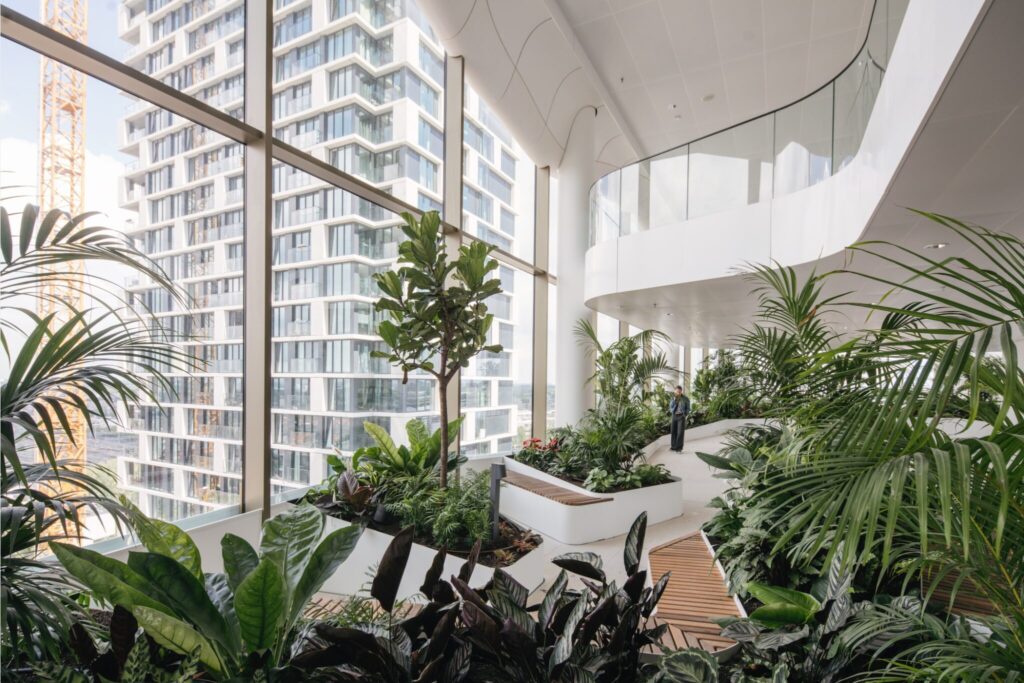 Biophilic interior design with lush tropical planting integrated into a modern high-rise building atrium with floor-to-ceiling windows.