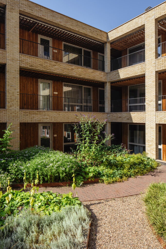 Groene binnentuin van Westbeat Amsterdam met biodivers beplantingsontwerp tussen houten en bakstenen gevels
