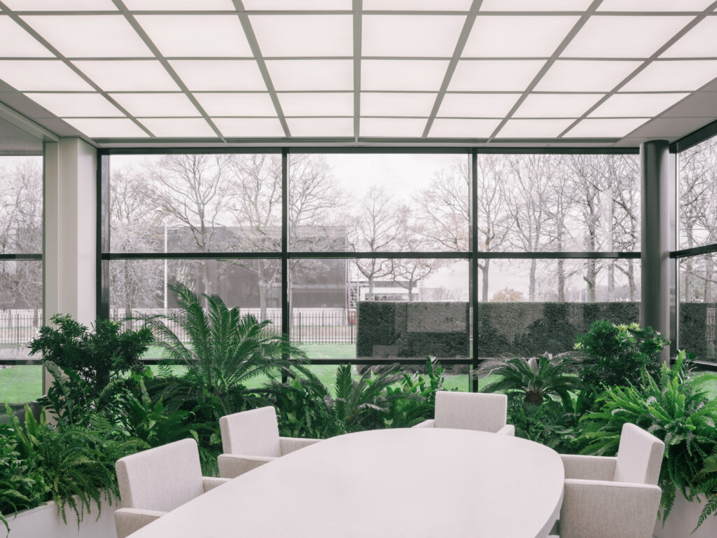 Meeting room overlooking lush indoor gardens with tropical plants and large windows at Elho headquarters in Tilburg, designed by MOSS.