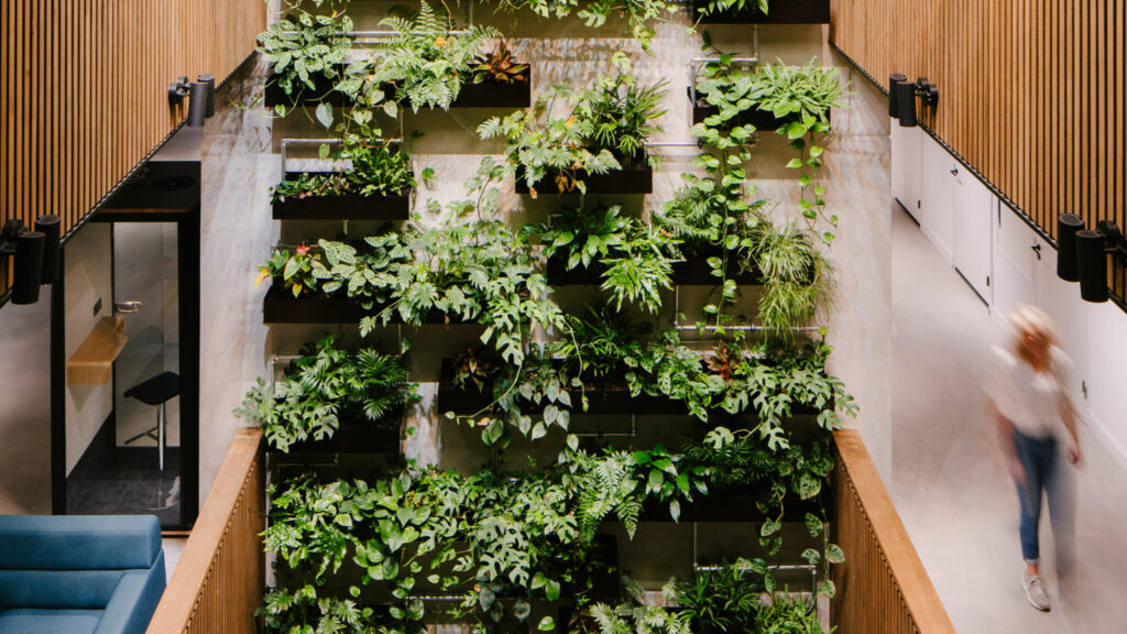 Four-story indoor green wall at Dura Vermeer Utrecht with cascading tropical plants and modular black planters in a sustainable office atrium.