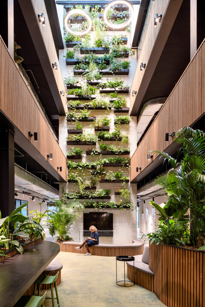 Biophilic atrium interior at Dura Vermeer Utrecht featuring a four-story living wall, natural daylight, wood finishes, and sustainable office design by MOSS Amsterdam.