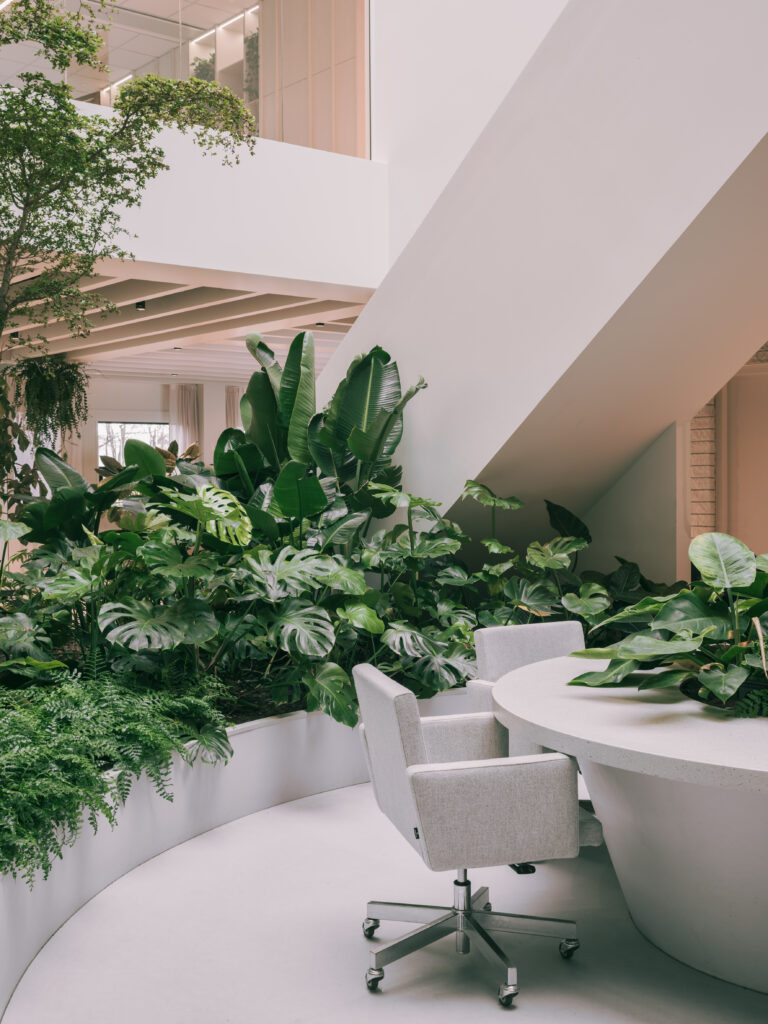Meeting area beneath a sculptural staircase surrounded by lush tropical planting at Elho headquarters in Tilburg, designed by MOSS using biophilic design principles.