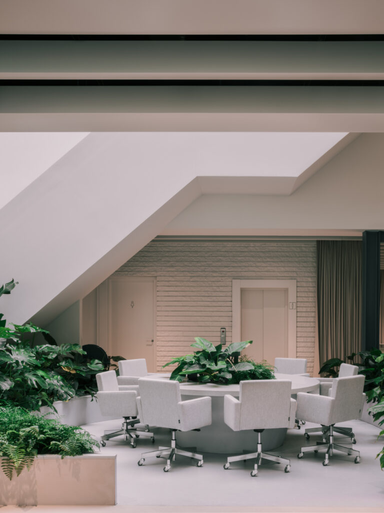 Alt Text Circular meeting table surrounded by integrated tropical planting beneath a sculptural staircase at Elho headquarters, designed by MOSS.