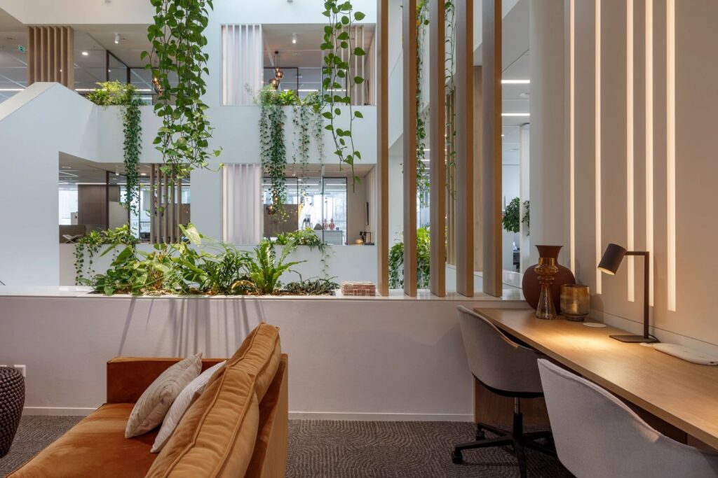 Biophilic office lounge at AM Office Amsterdam featuring cascading indoor plants, natural materials, and open atrium workspaces.