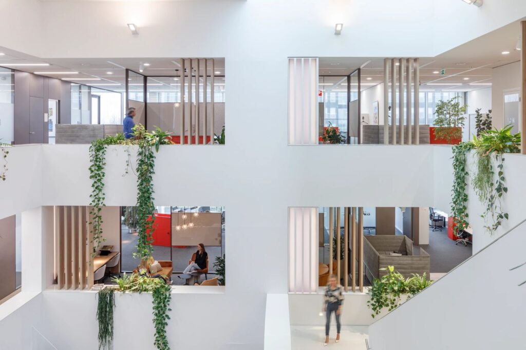 Open office atrium at AM Office Amsterdam with integrated planting, cascading vines, and collaborative workspaces across multiple floors.