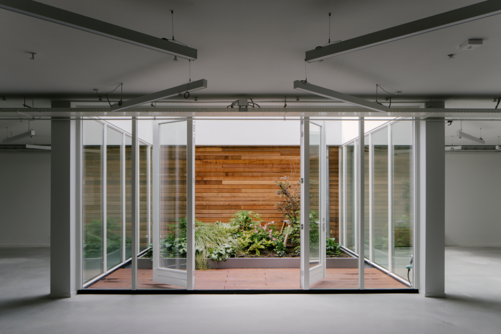 Glass doors opening to planted courtyard garden in renovated warehouse office at The Wearhouse Amsterdam