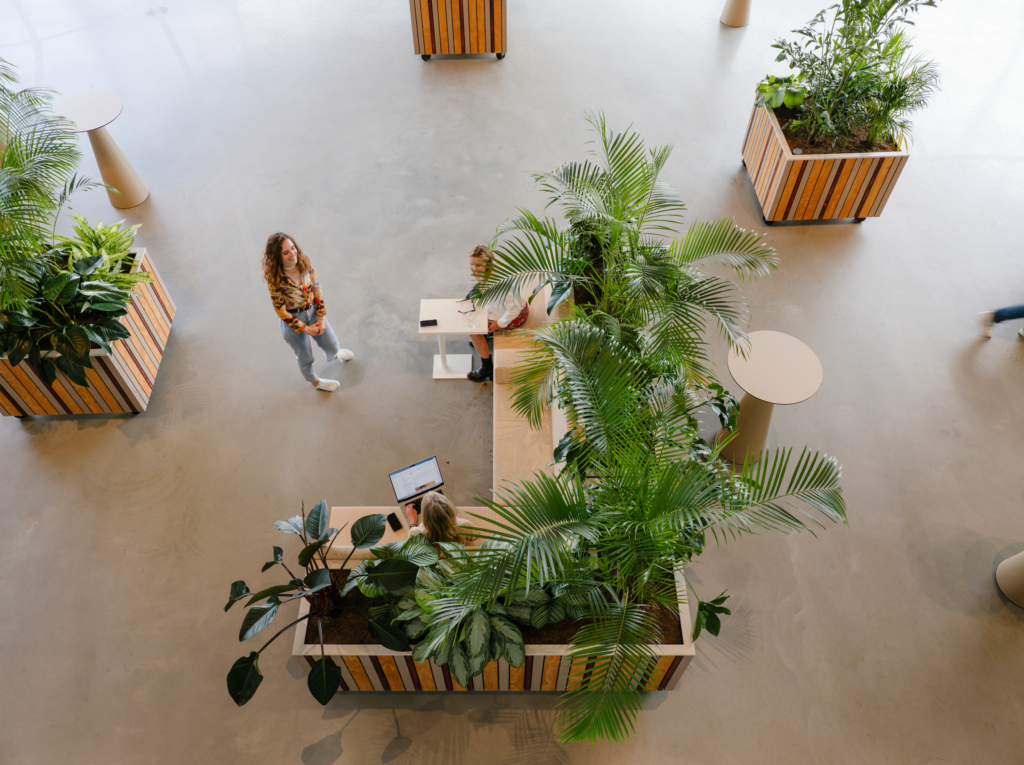 Visitors working beside lush modular planters filled with tropical indoor plants at Circa Amsterdam, creating flexible workspaces within a circular event venue.
