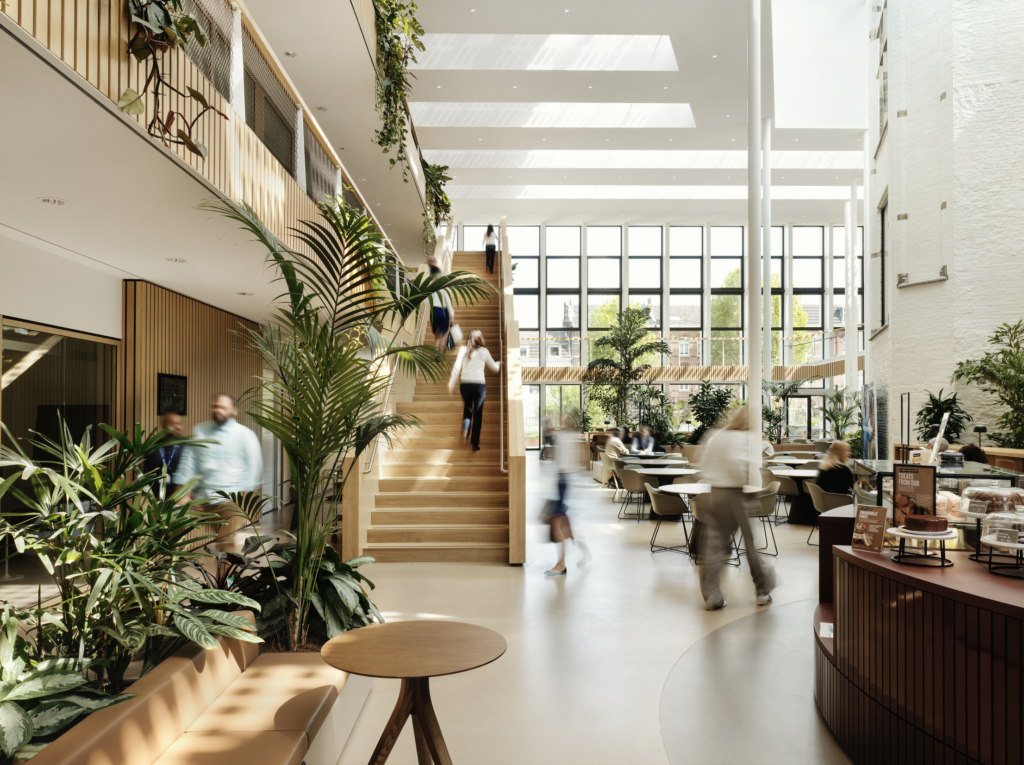 Central staircase in DSM-Firmenich Maastricht atrium with integrated planting, café seating, and natural daylight in a biophilic office environment