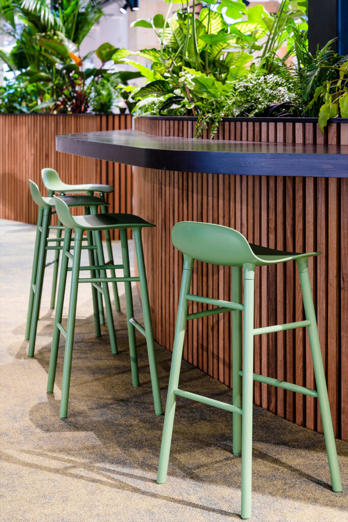 Biophilic office seating area at Dura Vermeer Utrecht featuring green bar stools, integrated wooden planters, and lush tropical indoor planting by MOSS Amsterdam.