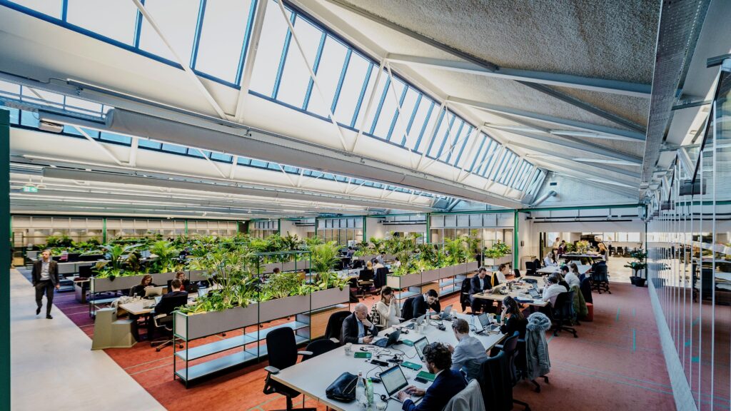 Panoramic view of The Core Amsterdam showing open workspaces, integrated tropical planting, greenhouse meeting rooms, and abundant natural daylight.