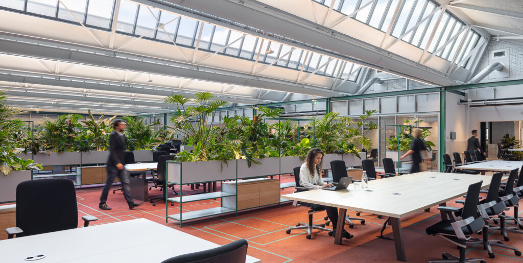 Employees working in an open collaborative office surrounded by integrated tropical planting at The Core Amsterdam by MOSS.