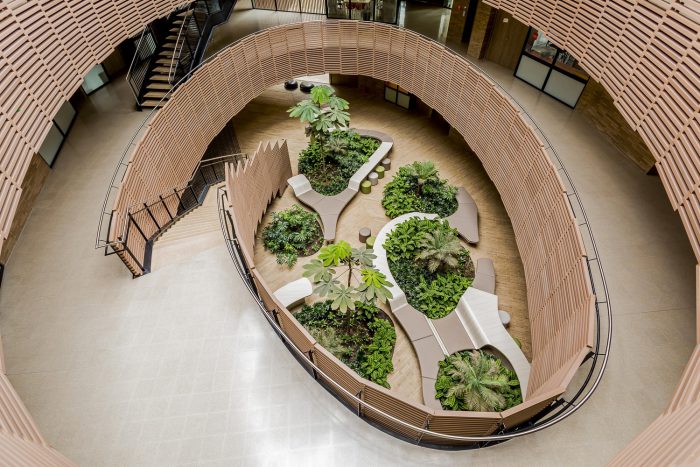 Biophilic office atrium with curved timber architecture, integrated indoor planting beds, and lush greenery designed to enhance wellbeing, biodiversity, and employee experience.