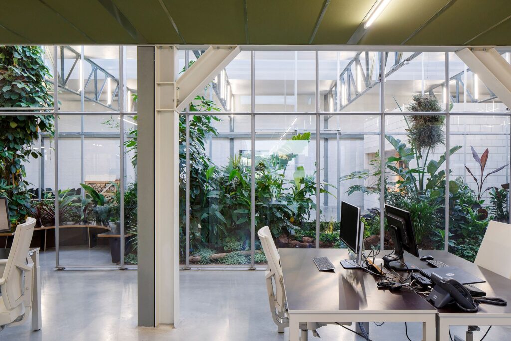Biophilic office interior with glass walls and indoor garden, promoting employee well-being and green workplace design