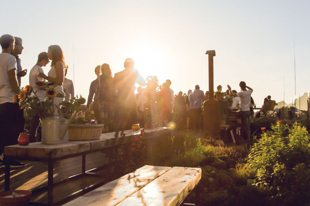 People dining on NEST rooftop garden at Casa400 hotel Amsterdam during sunset surrounded by edible plants designed by MOSS Amsterdam